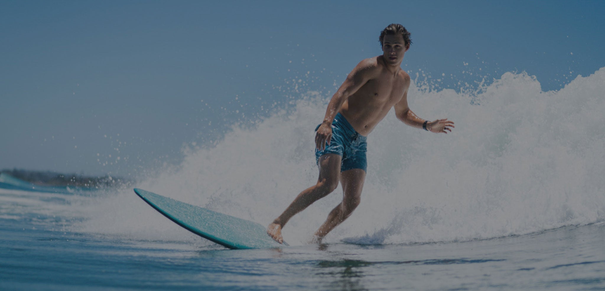 Water shot of guy performing bottom turn on a longboard while wearing trunks 