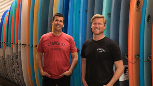 Degree 33 owner standing in front of a colorful row of surfboards of all different sizes